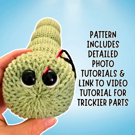 Hand holding a green crochet caterpillar amigurumi plush with large safety eyes, blue background.