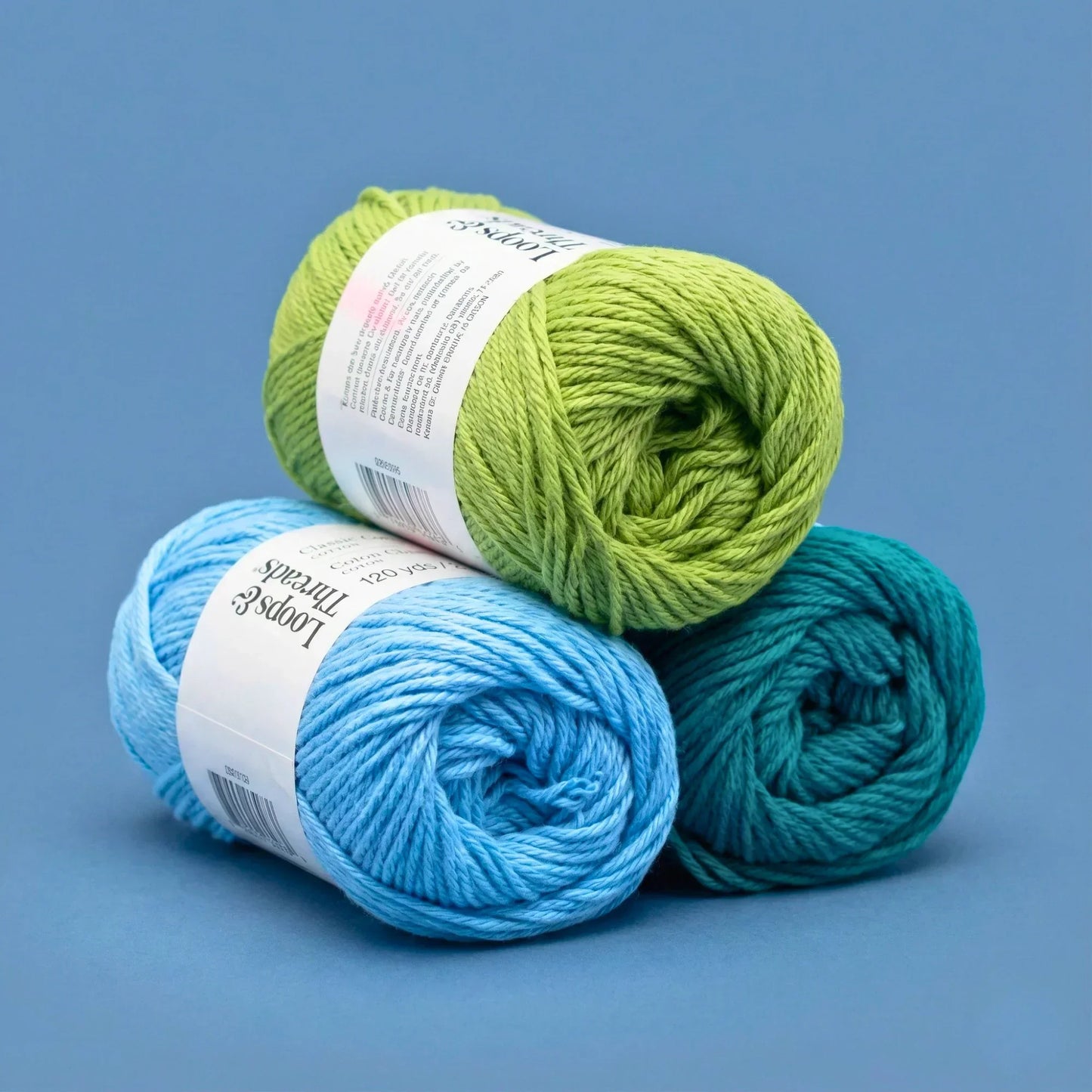 Three skeins of colorful yarn for crochet in green, blue, and teal on a blue background