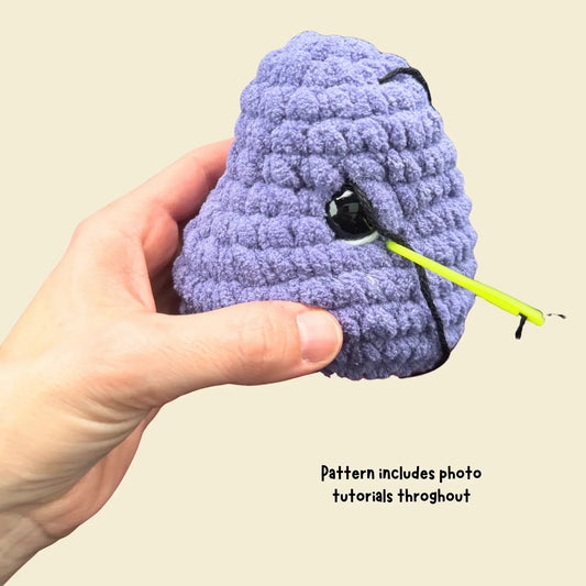 Hand holding purple crochet brontosaurus head, safety eye inserted, amigurumi tutorial guide.