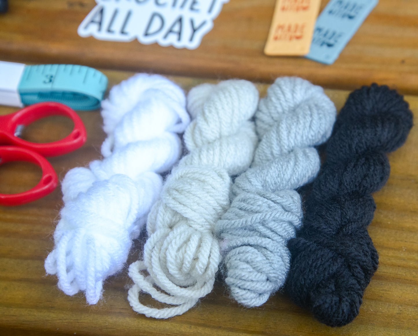 Four balls of yarn in white, gray, and black on a wooden surface with scissors.