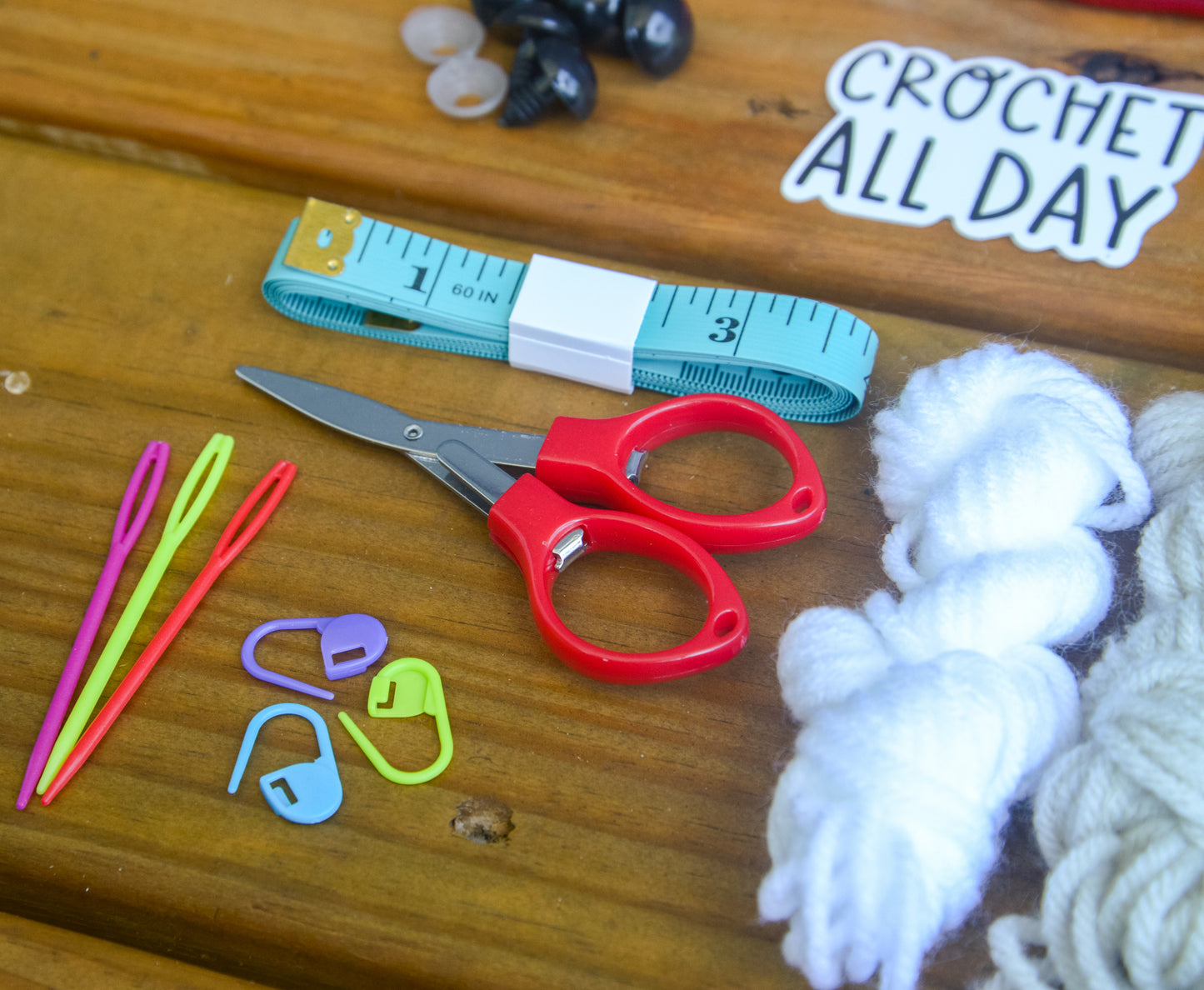 Craft supplies including scissors, yarn, and measuring tape on a wooden surface with 'Crochet All Day' sign.