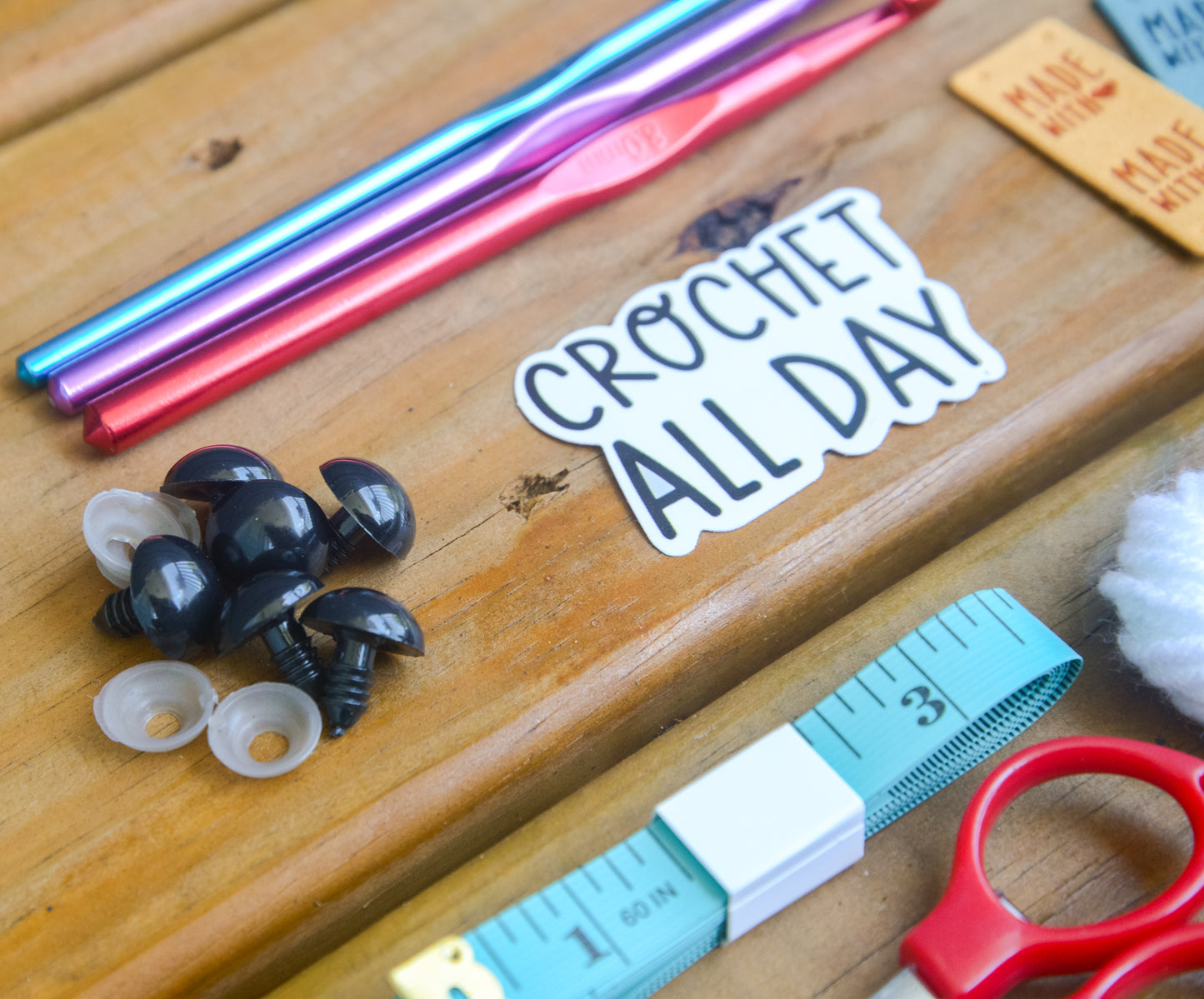 Crochet tools and accessories on a wooden surface with a 'Crochet All Day' sticker.