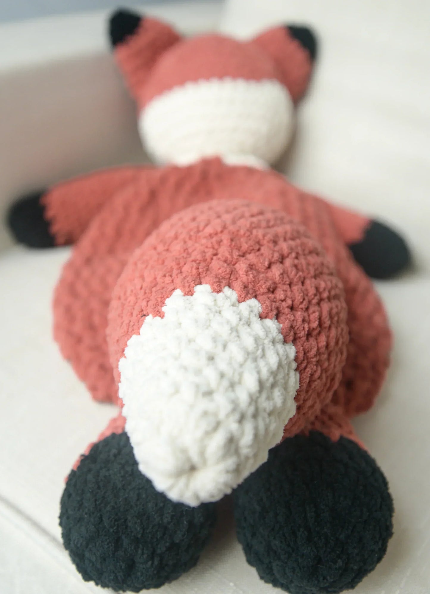 Plush crochet fox stuffed animal with white tail and black paws on a cream couch