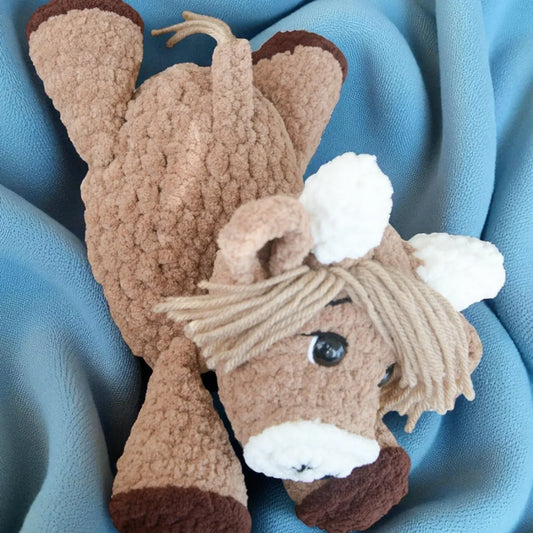 Handmade crochet Highland cow plushie with yarn hair on a blue blanket