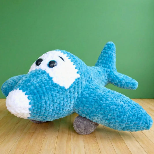 Blue crochet airplane plushie toy with white details and big eyes on wood floor