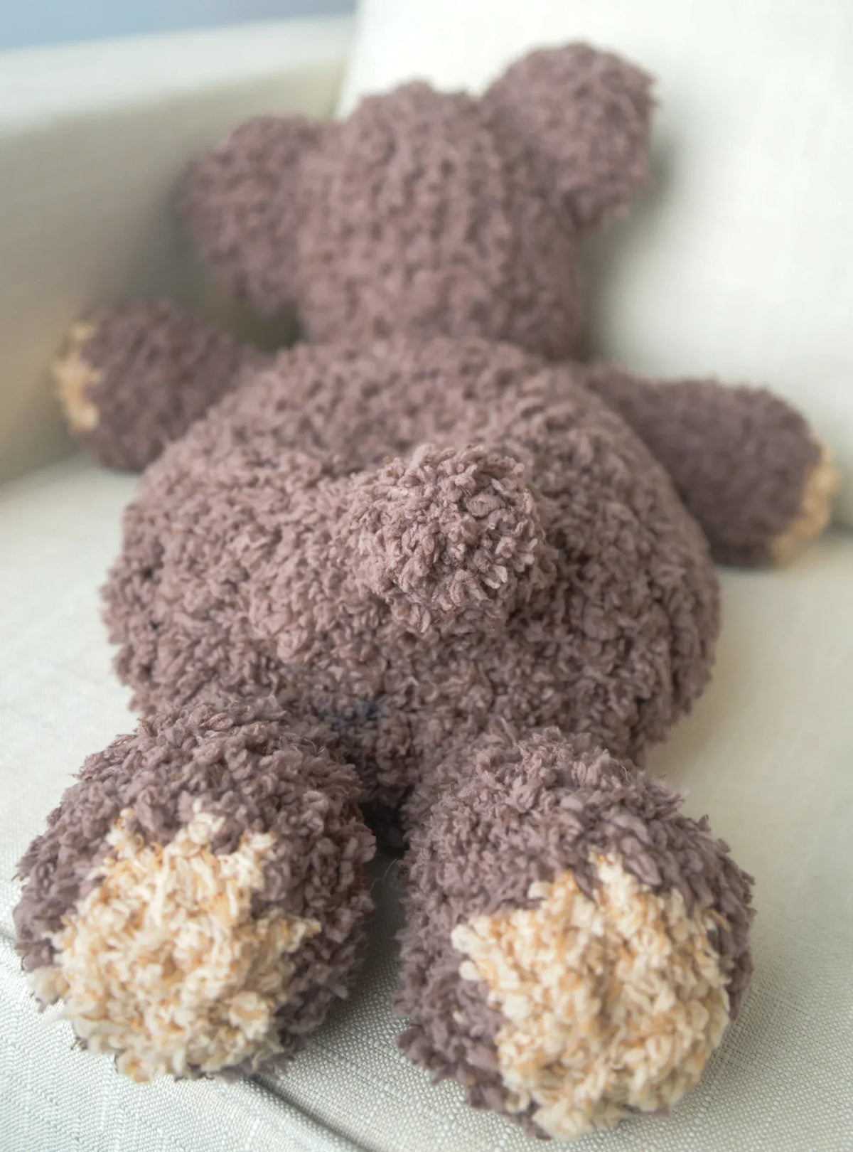Handmade crochet bear plushie with textured brown yarn lying on a cream sofa.