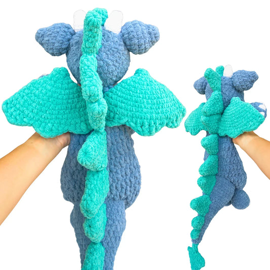 Hand holding a plush crochet dragon with teal wings and tail, amigurumi stuffed animal toy