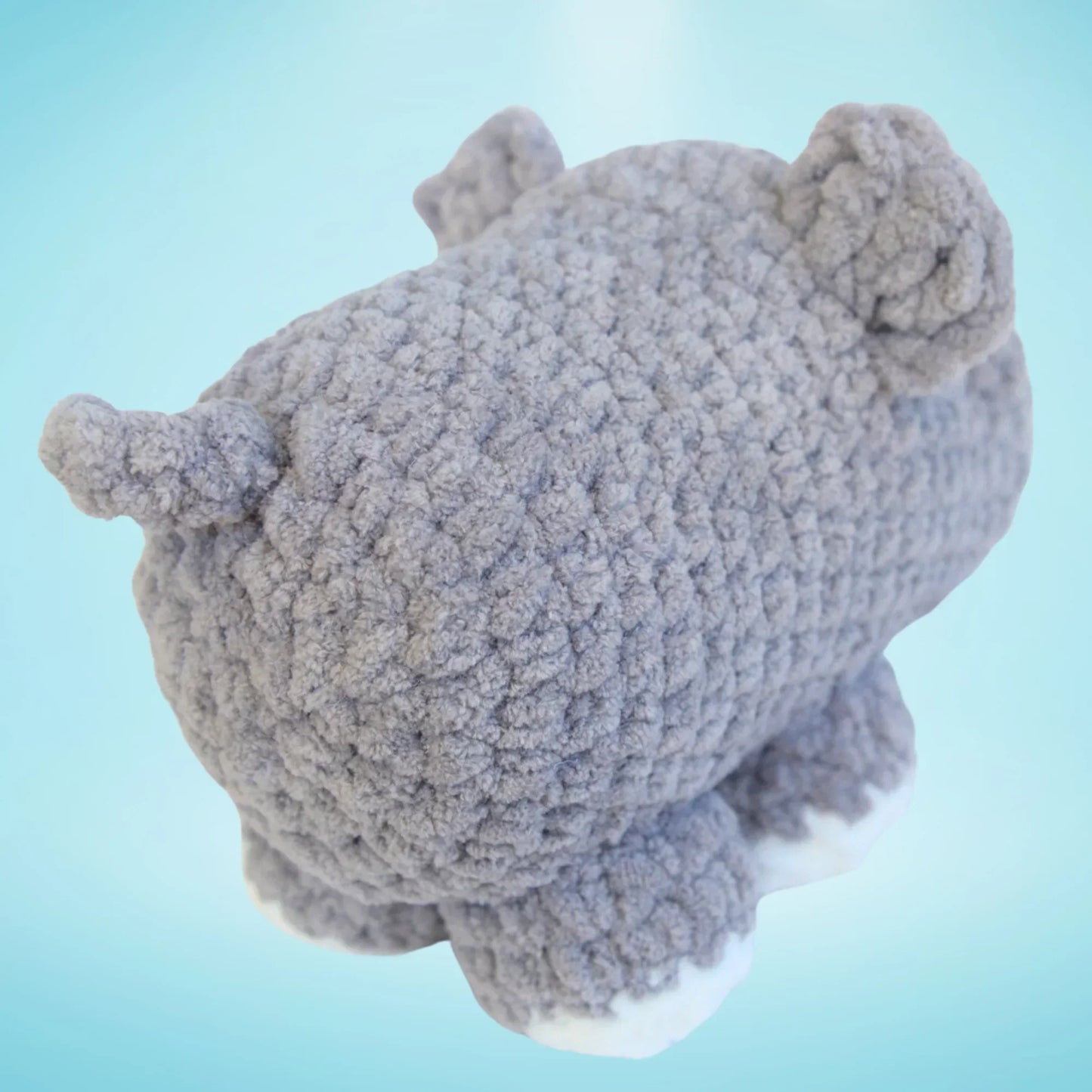 Plush grey crochet hippo amigurumi toy with white feet on blue background
