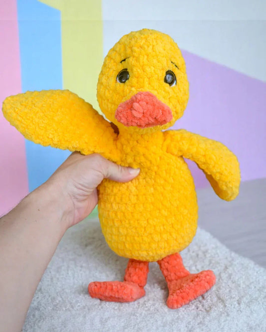 Hand holding a yellow crochet duck plushie with orange beak and feet, amigurumi toy