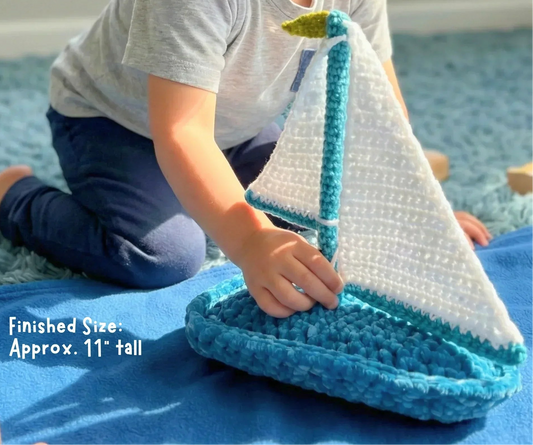 Child playing with handmade crochet sailboat toy on blue rug, finished size 11 inches tall