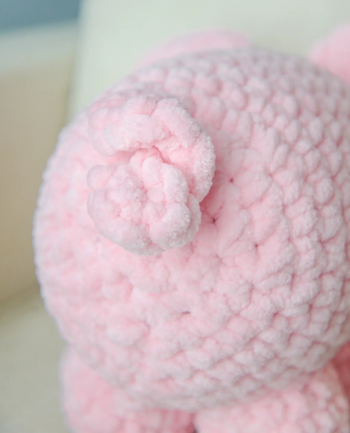 Close-up of a pink crochet stuffed pig with a curly tail, plush amigurumi toy