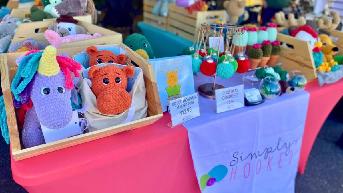 Colorful crochet stuffed animals, plushies, and ornaments displayed at a craft market table.