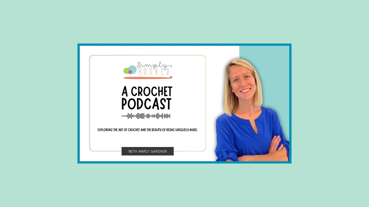 A smiling woman in blue stands beside a sign reading 'A Crochet Podcast, exploring the art of crochet.'