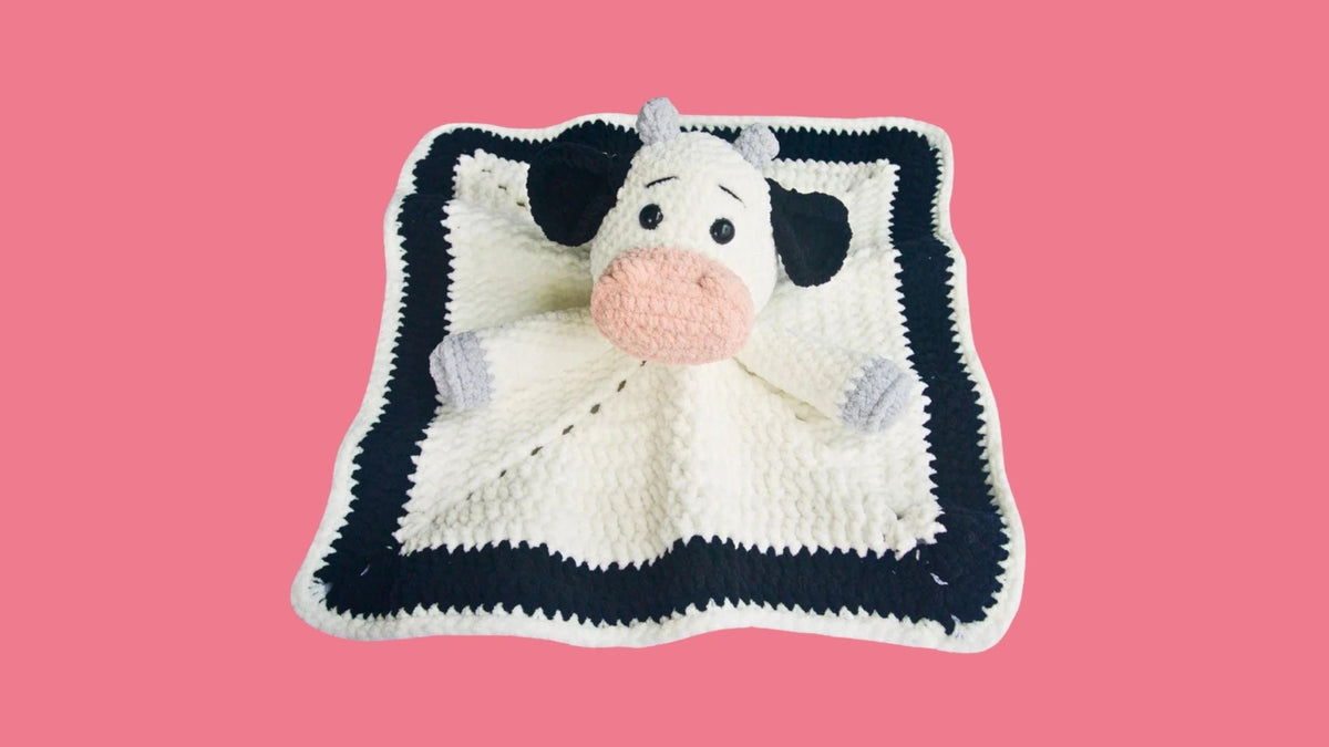 Crochet cow lovey blanket with black border on pink background, amigurumi plushie pattern
