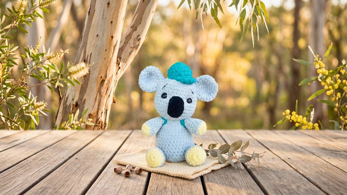 Crochet koala plushie amigurumi on wooden deck with forest background