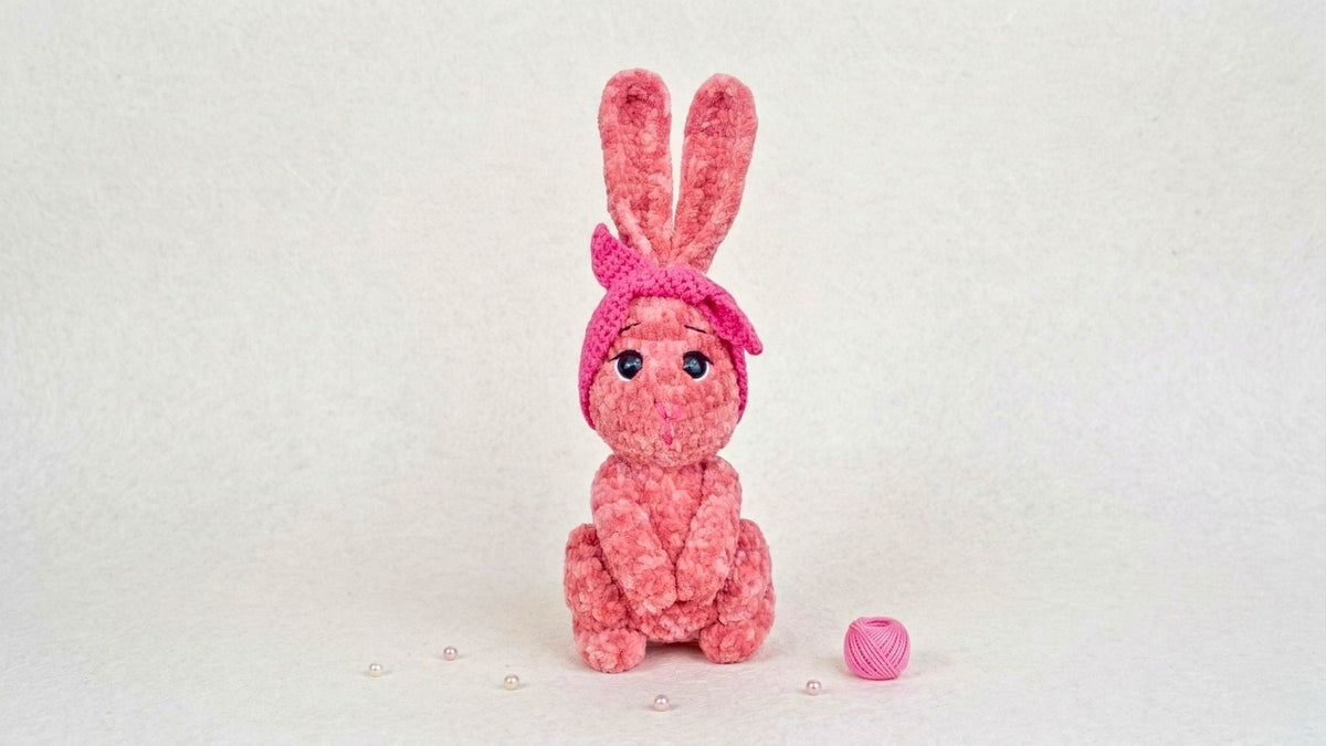 Pink crochet bunny plushie with a bow, amigurumi stuffed animal, on a white background