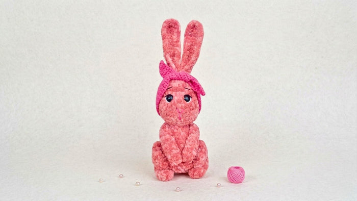 Pink crochet bunny plushie with a bow, amigurumi stuffed animal, on a white background