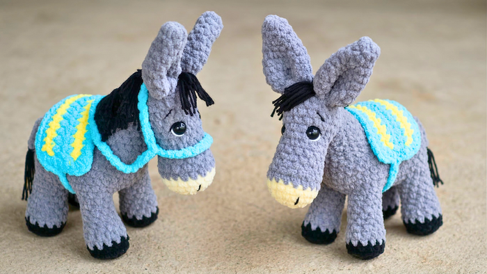 Two crochet donkey plushies with blue and yellow saddles on a beige background