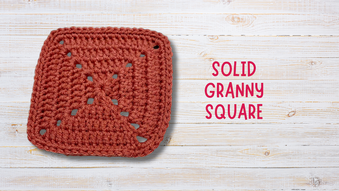 Crochet solid granny square in rust yarn on white wood background, text reading solid granny square.