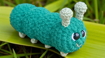 Handmade crochet caterpillar plushie with big eyes on a green leaf, amigurumi pattern