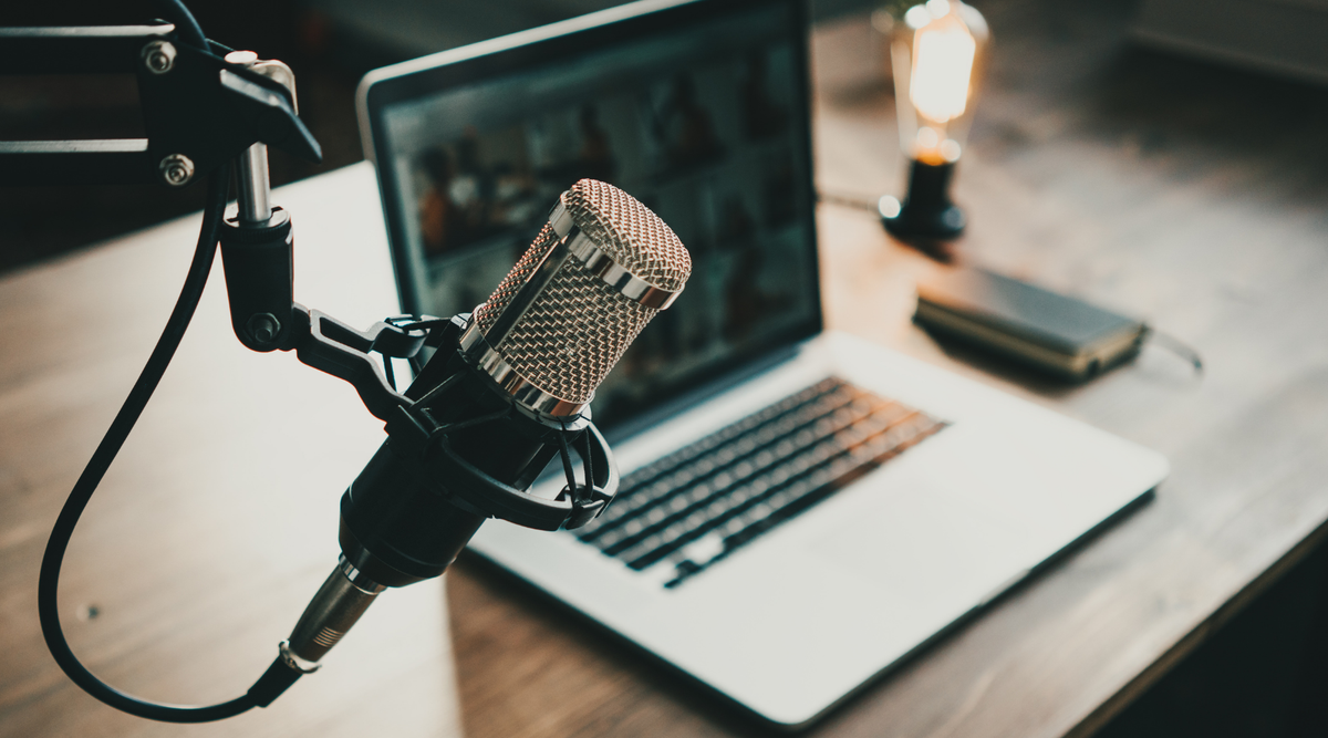 Podcast microphone and laptop on wooden desk with warm lighting, creative workspace setup