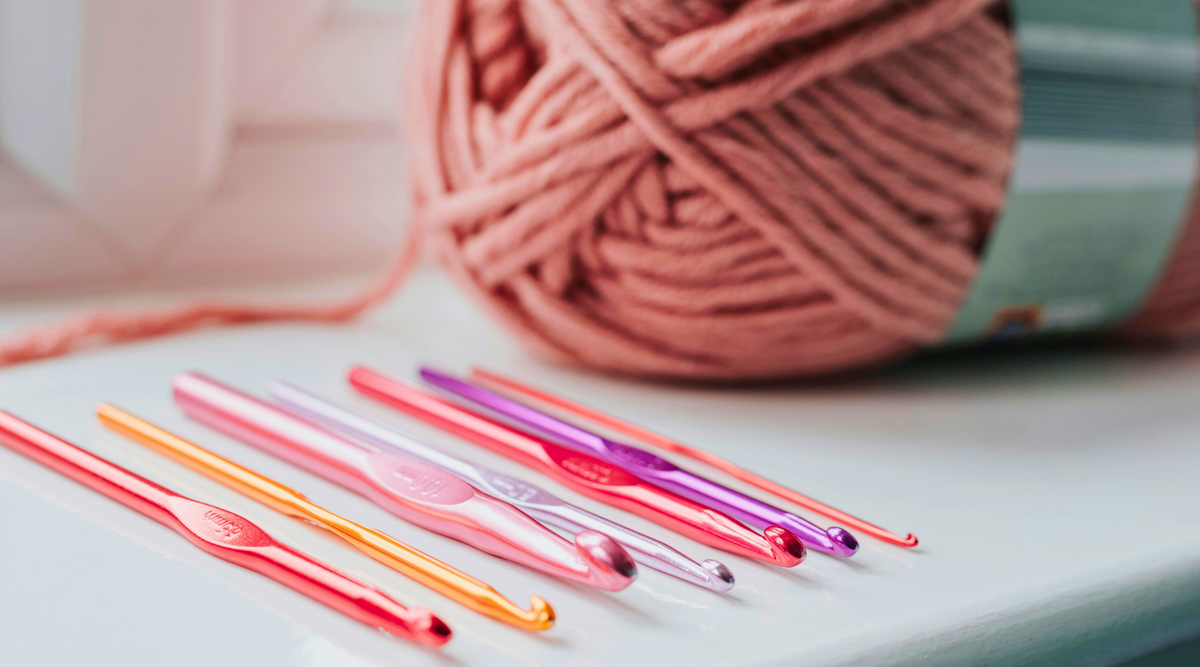 Colorful crochet hooks and pink yarn ball on white surface, beginner crochet tools