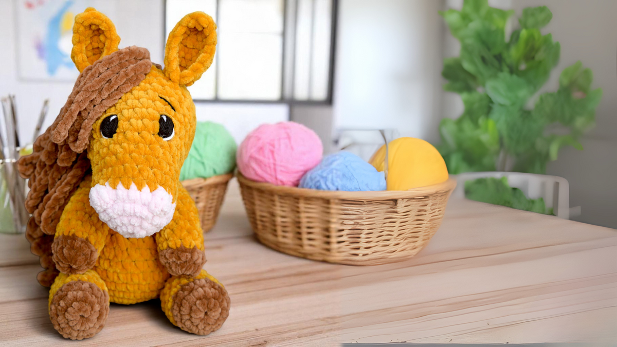 crochet horse plushie with brown mane, sitting near baskets of colorful yarn on a table