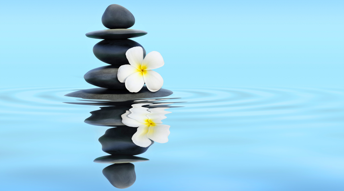 Stacked black spa stones with a white frangipani flower on calm blue water background