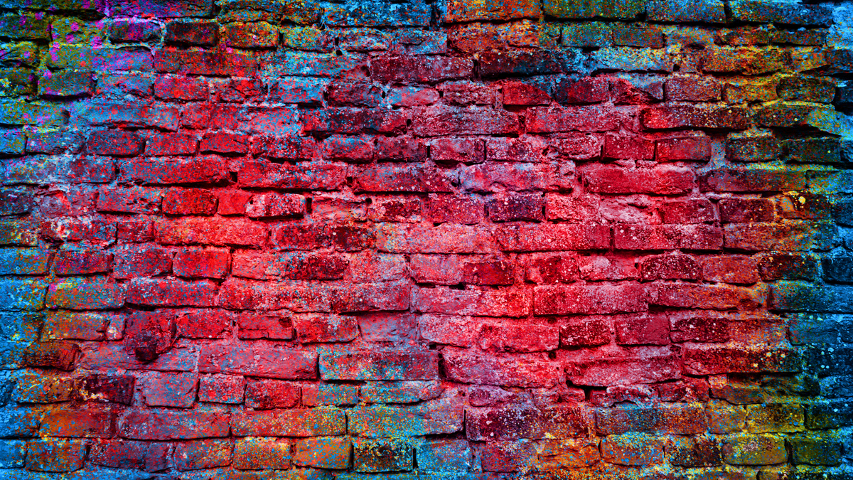 Red brick wall with vivid multicolored paint splashes and textured surface.