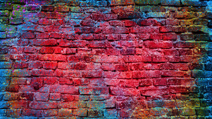 Red brick wall with vivid multicolored paint splashes and textured surface.