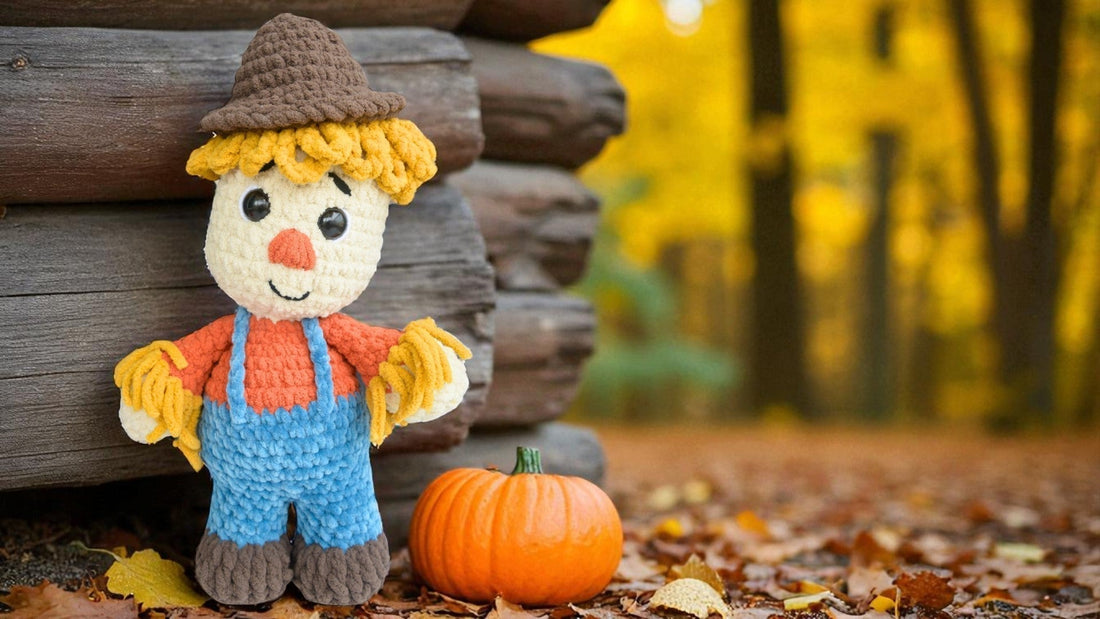 Crocheted scarecrow plushie with orange shirt, blue overalls, and brown hat next to a small pumpkin outdoors