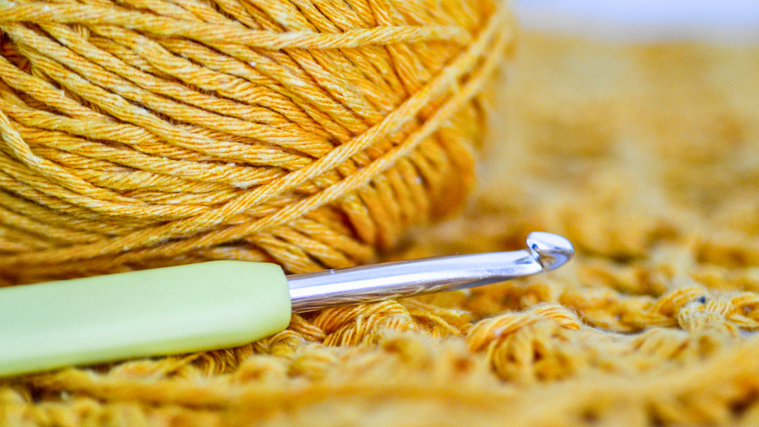 Close-up of yellow yarn ball and metal crochet hook on textured crochet fabric