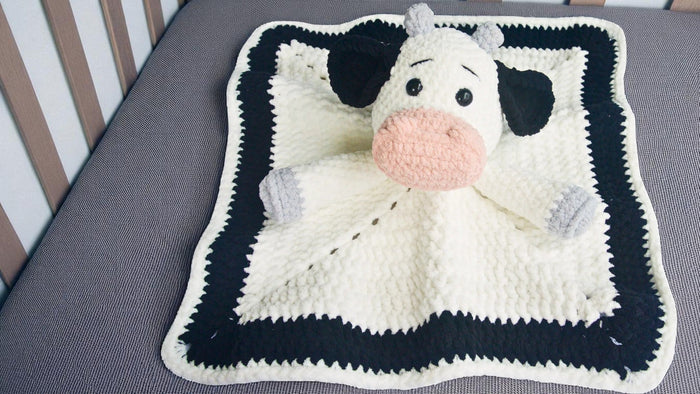Soft crocheted black and white cow baby blanket on gray crib mattress