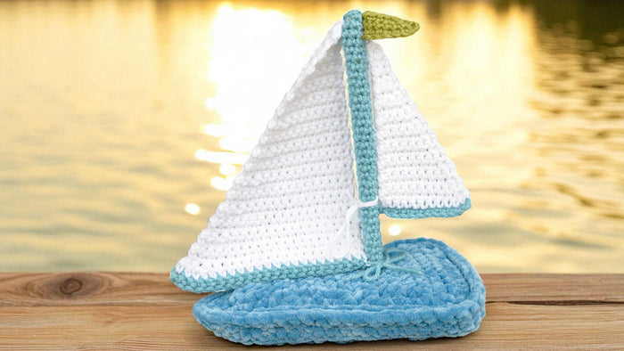 crocheted sailboat toy with white and blue sails on wooden dock by golden water