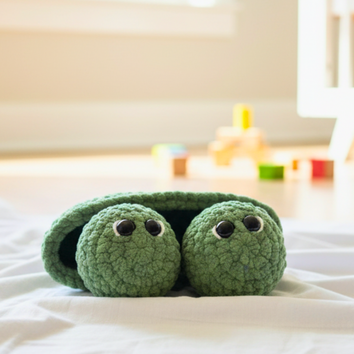 Soft green crocheted turtle toy with big eyes on a white surface in a bright playroom