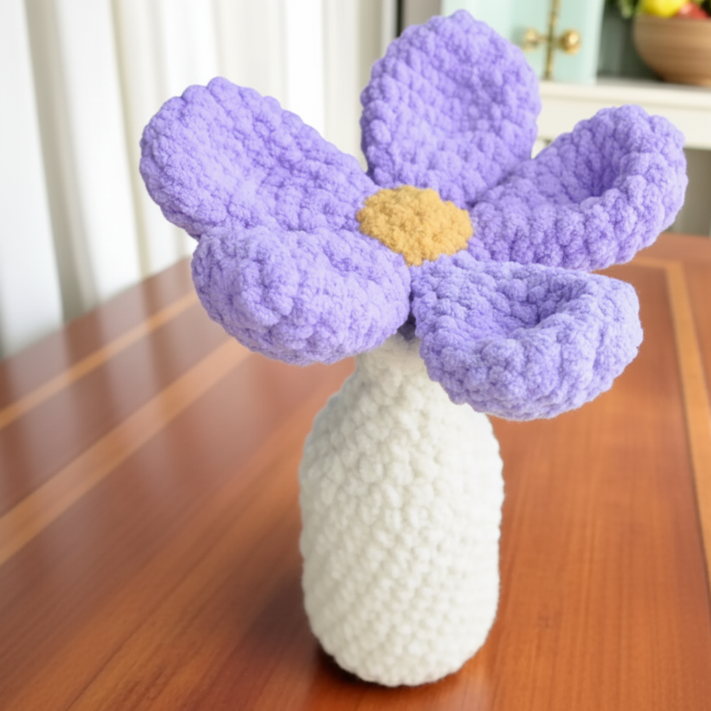 Handmade crochet purple flower with yellow center in white vase on wooden table