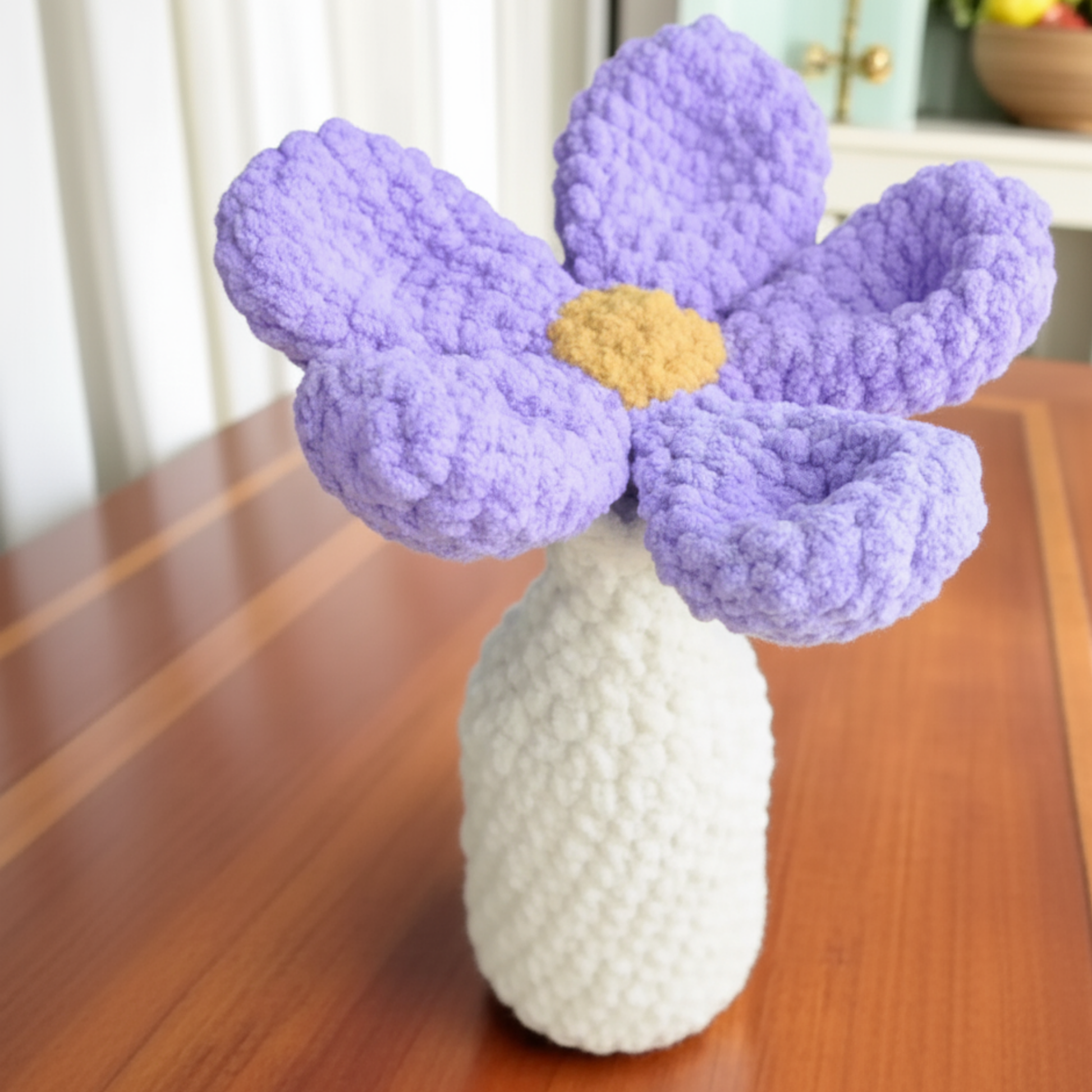 Handmade crochet purple flower with yellow center in white vase on wooden table