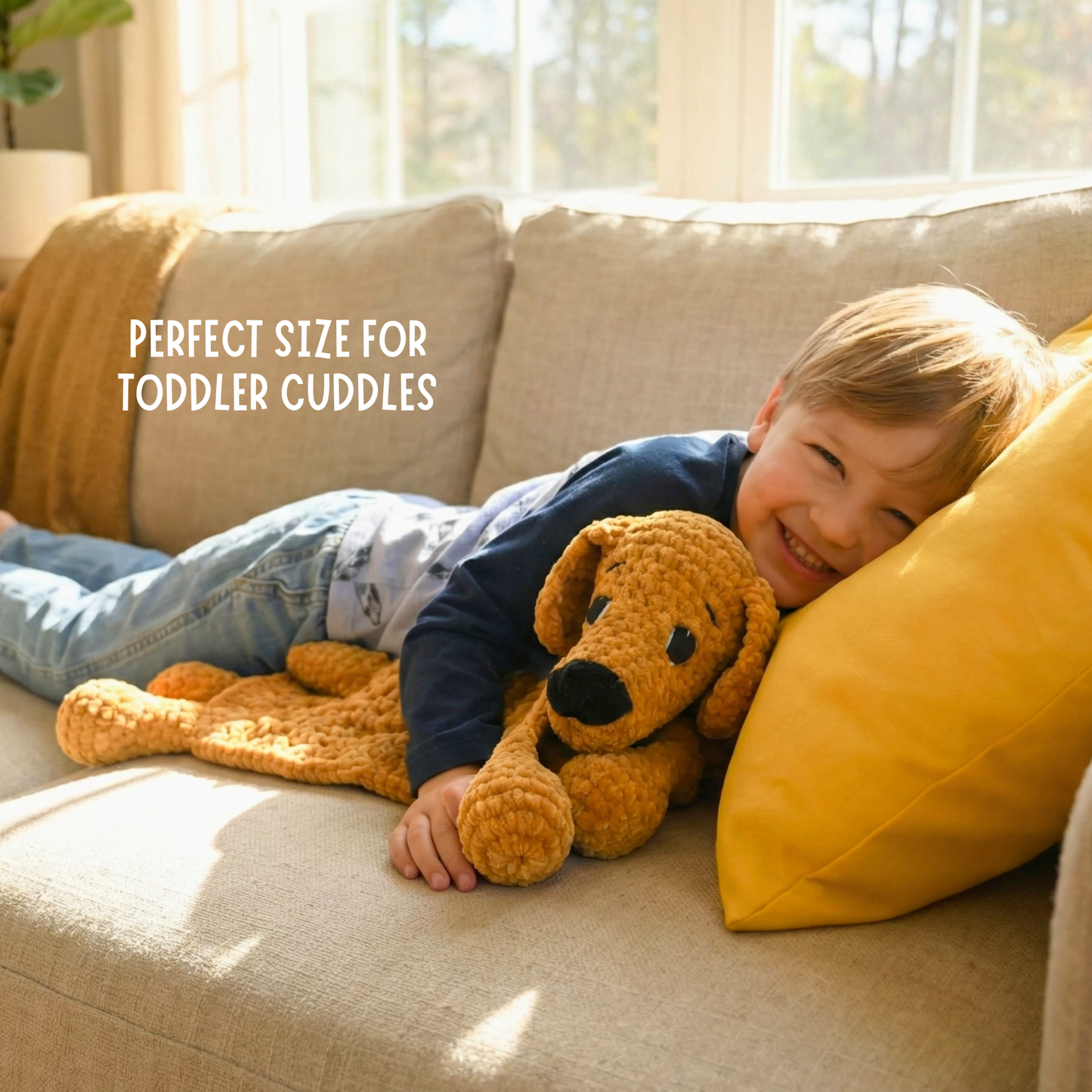Smiling toddler cuddling a plush dog blanket on beige couch with yellow pillow in sunlit room