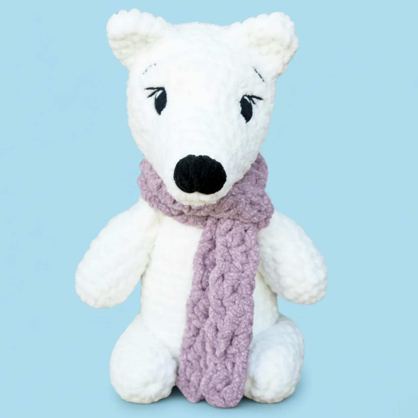 White crocheted polar bear plush with black nose and eyes wearing a purple knitted scarf