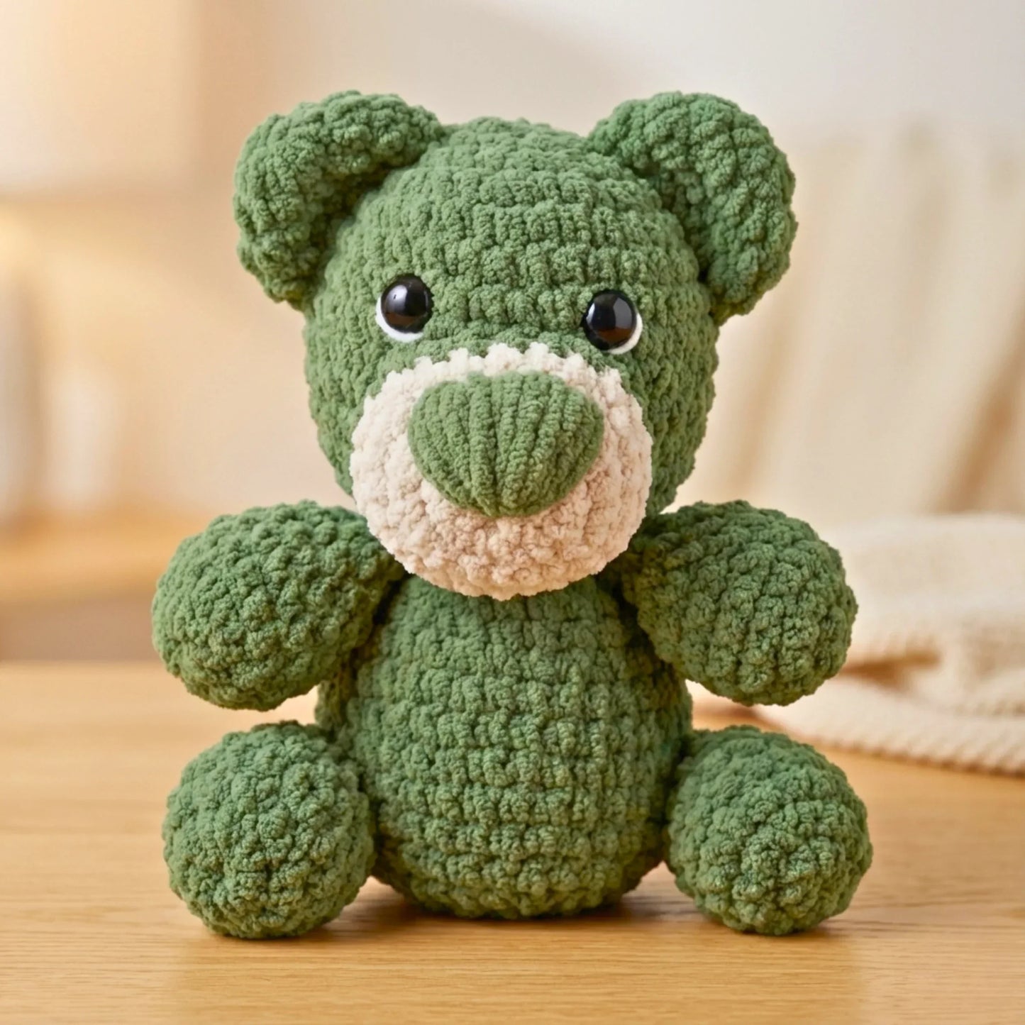 Green crochet teddy bear plushie with big eyes, sitting on a wooden surface