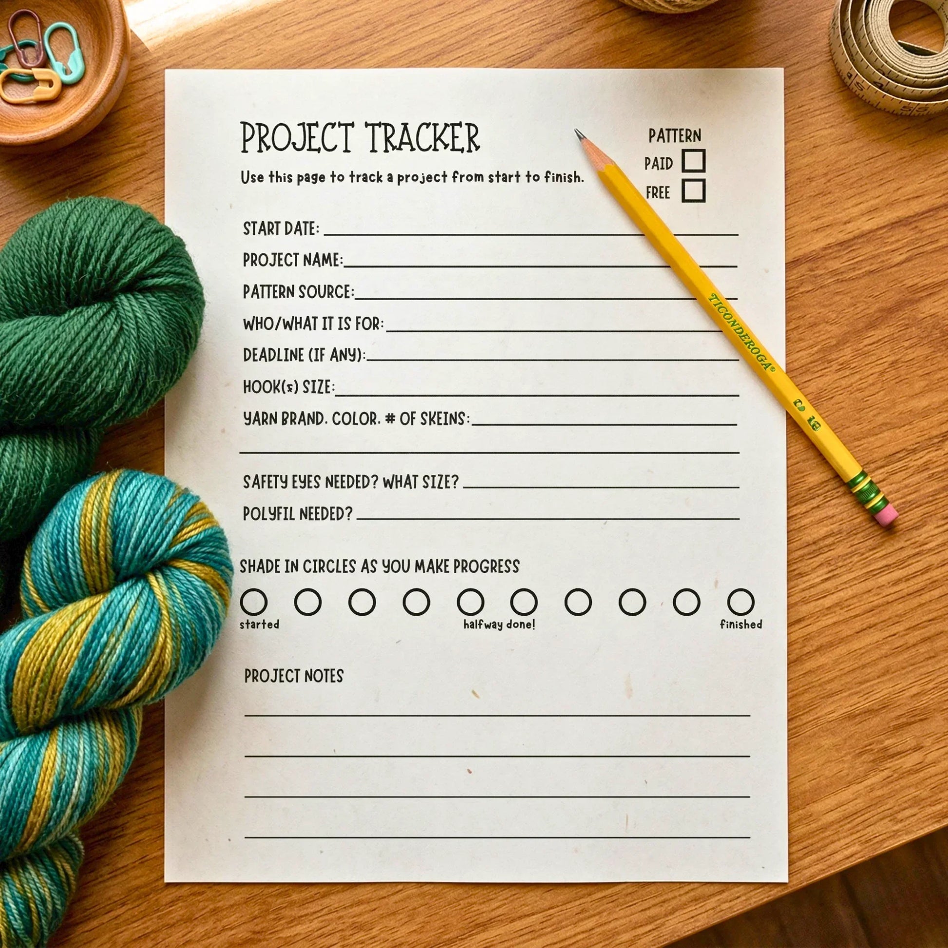 Crochet project tracker printable with pencil, yarn skeins, and craft supplies on wooden table