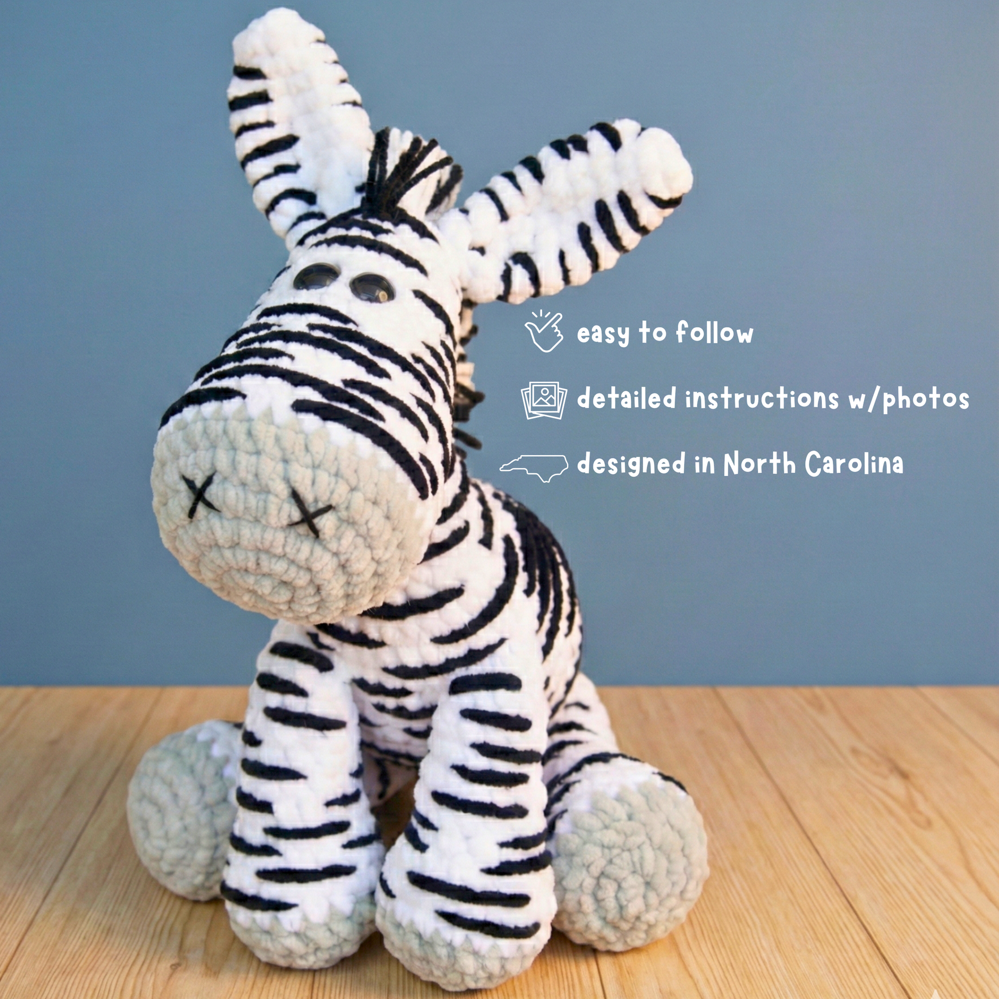 Handmade crocheted zebra plush sitting on wooden floor with blue background and design details text