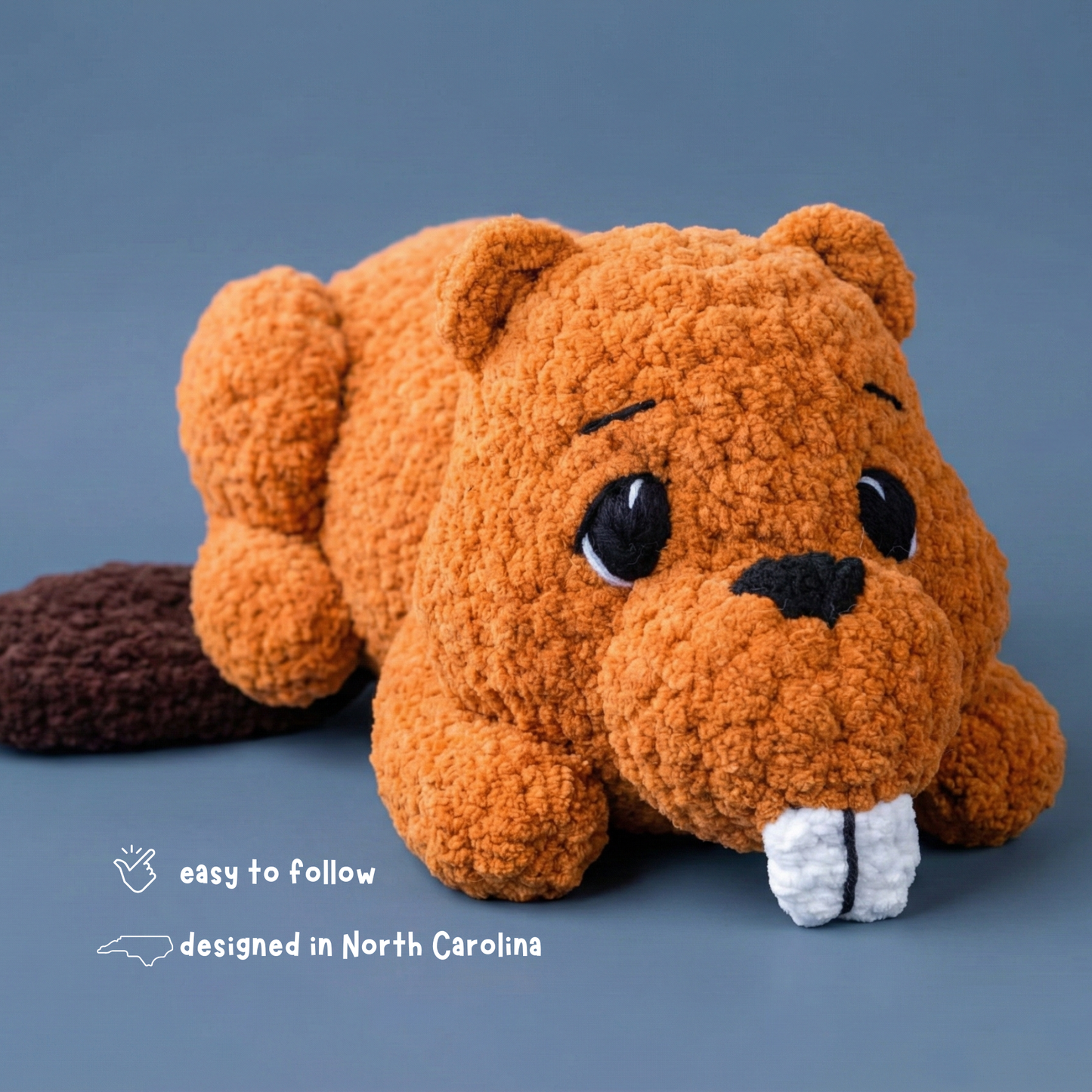 Plush crochet beaver toy with big eyes and buck teeth on blue background, designed in North Carolina