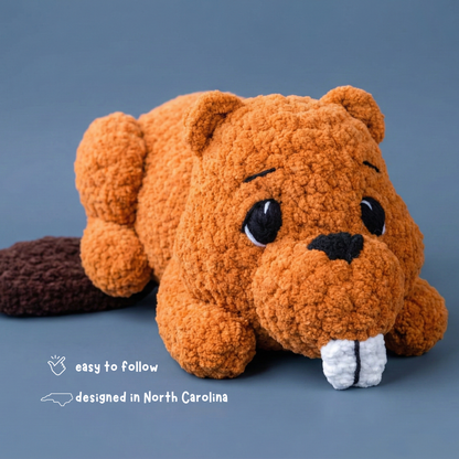 Plush crochet beaver toy with big eyes and buck teeth on blue background, designed in North Carolina