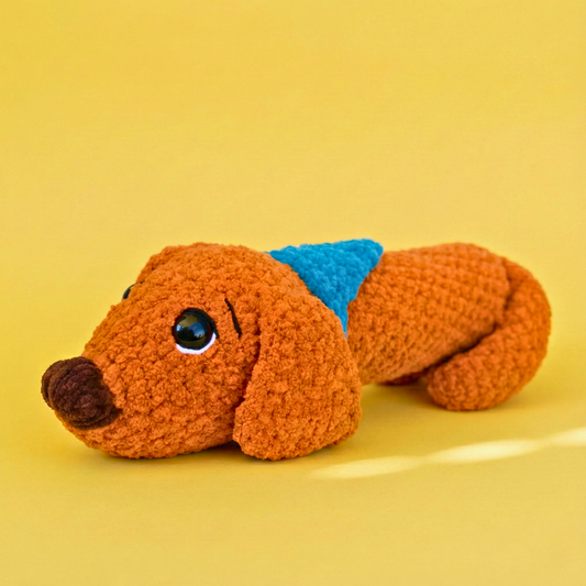 Handmade brown crochet dachshund stuffed toy with blue collar on yellow background
