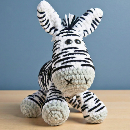 Handmade crocheted zebra stuffed animal with black stripes on white yarn sitting on wooden surface