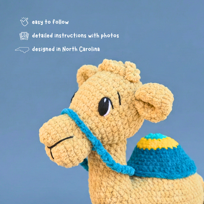 Handmade crocheted camel toy with blue saddle against blue background, easy crochet pattern