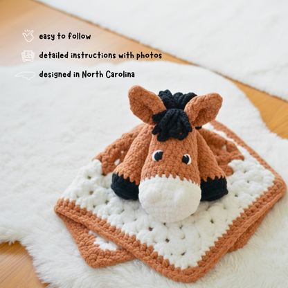 Crocheted horse lovey with brown, black, and white yarn on soft white blanket