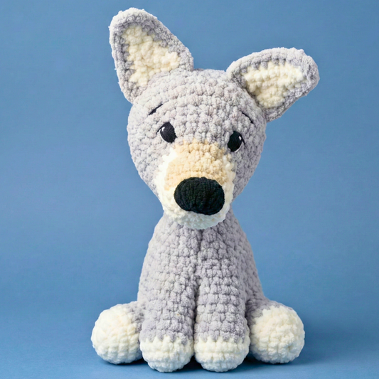 Handmade plush grey and white crochet dog toy sitting against blue background