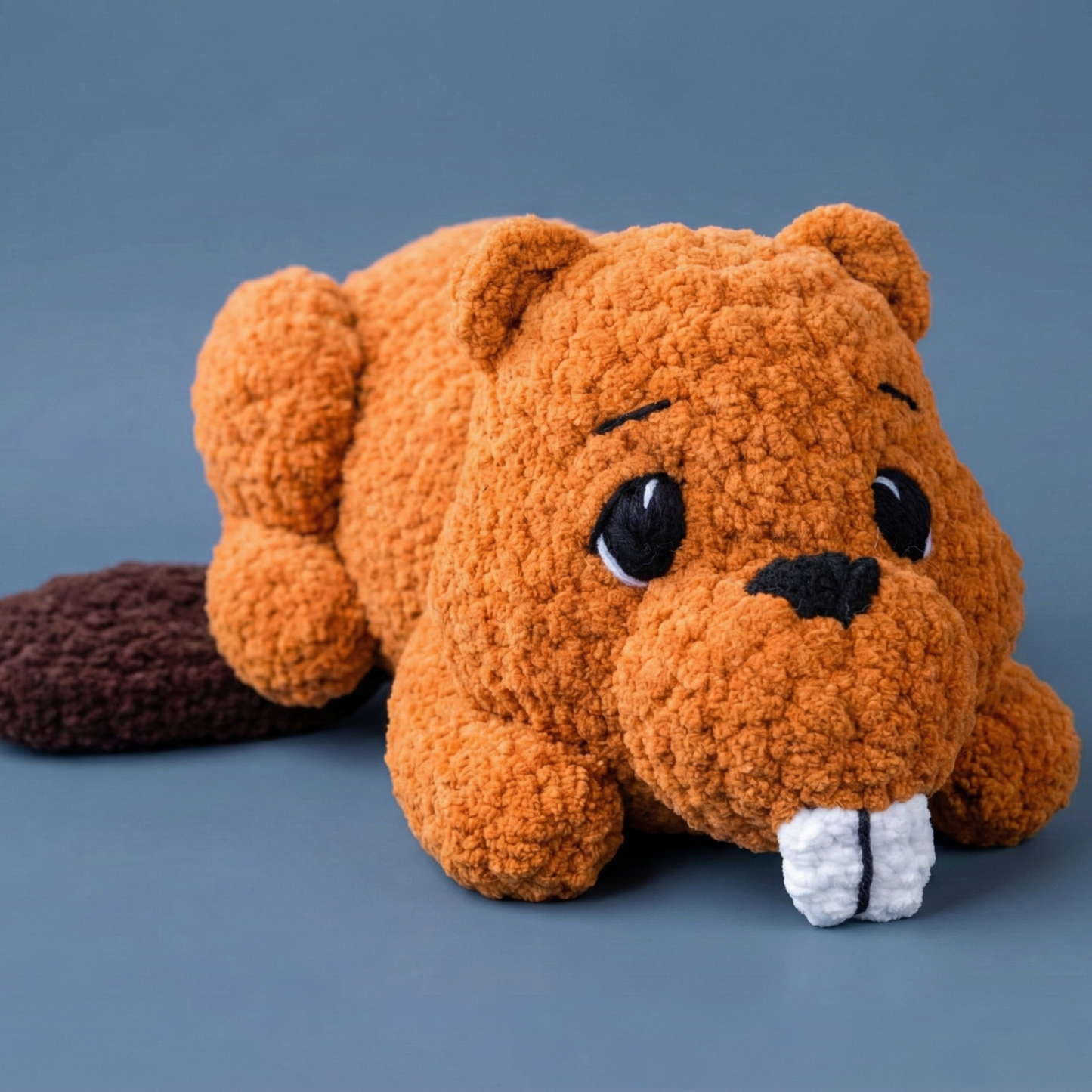 Cute brown crocheted beaver plush toy with large white teeth on blue background